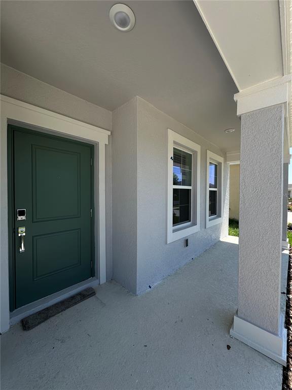 A covered front porch features a dark green door, two windows, and a concrete floor — 4039 AMBROSE AVENUE, KISSIMMEE, FL