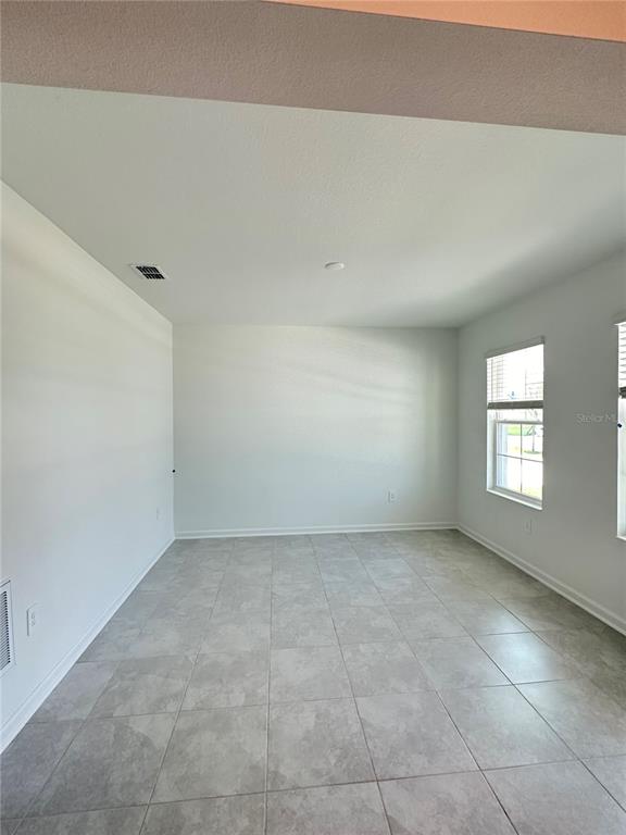 A bright, empty room features light gray tile flooring, white walls, and two windows — 4039 AMBROSE AVENUE, KISSIMMEE, FL