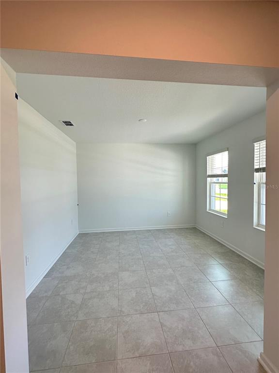 An empty room with light-colored tile flooring, white walls, and two windows — 4039 AMBROSE AVENUE, KISSIMMEE, FL