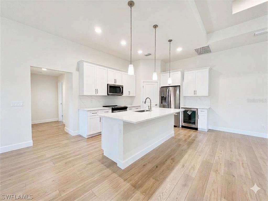 A modern kitchen features white cabinetry, a central island, stainless steel appliances, and wood flooring — 7 KASHGAR COURT, PALM COAST, FL