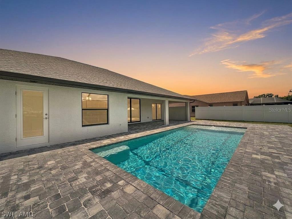 A rectangular swimming pool sits on a stone patio behind a white house at sunset — 7 KASHGAR COURT, PALM COAST, FL