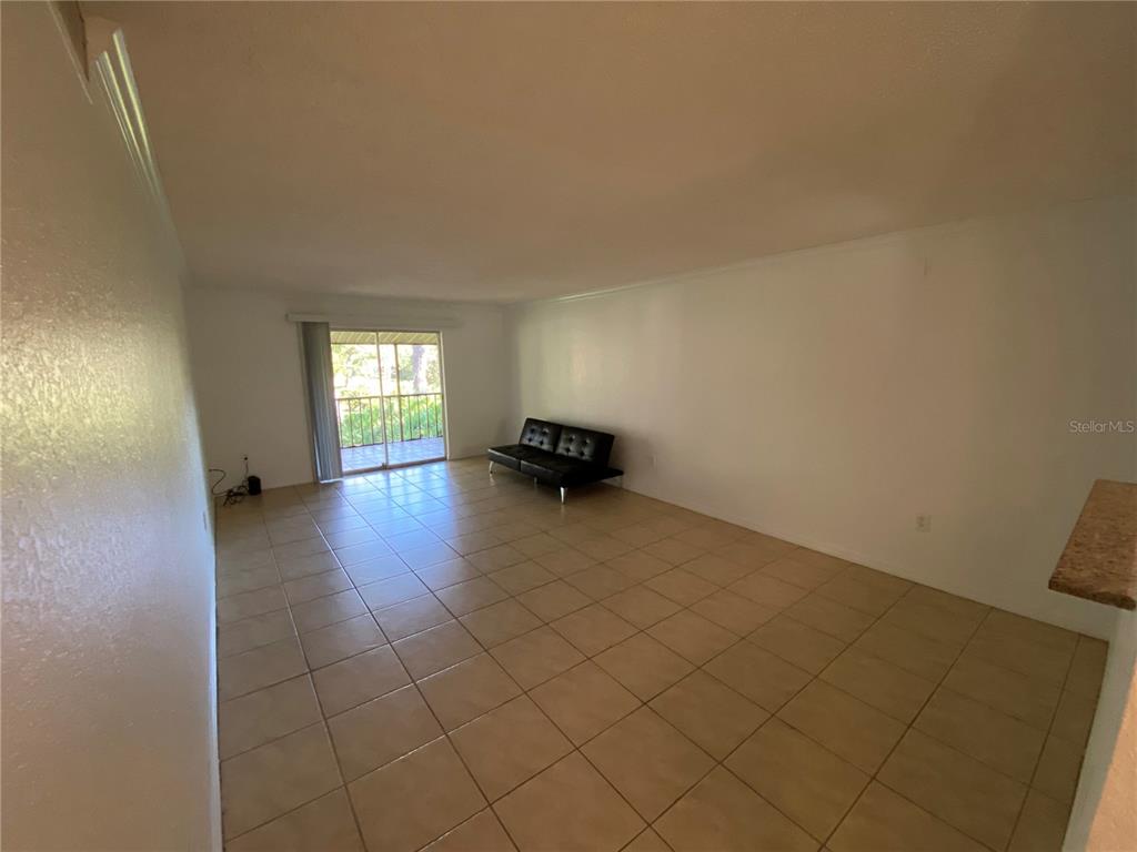 An empty living room features beige floor tiles, white walls, and a sliding glass door — 972 LA COSTA CIRCLE UNIT 8, SARASOTA, FL