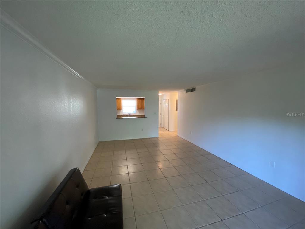 A living room with light-colored tile flooring and a pass-through window to the kitchen — 972 LA COSTA CIRCLE UNIT 8, SARASOTA, FL
