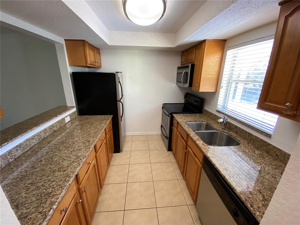 A galley kitchen features wood cabinets, granite countertops, tile flooring, and stainless steel appliances — 972 LA COSTA CIRCLE UNIT 8, SARASOTA, FL