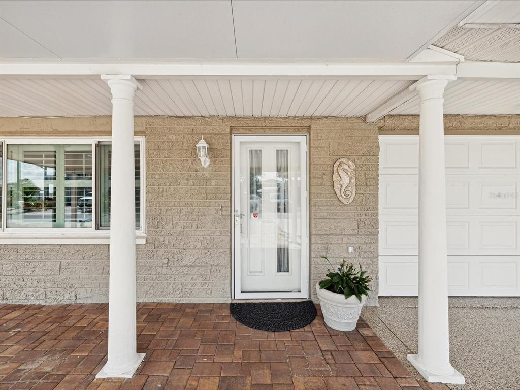 A covered porch with brick pavers, white columns, and a front door with a storm door — 13521 VERONICA DRIVE, HUDSON, FL