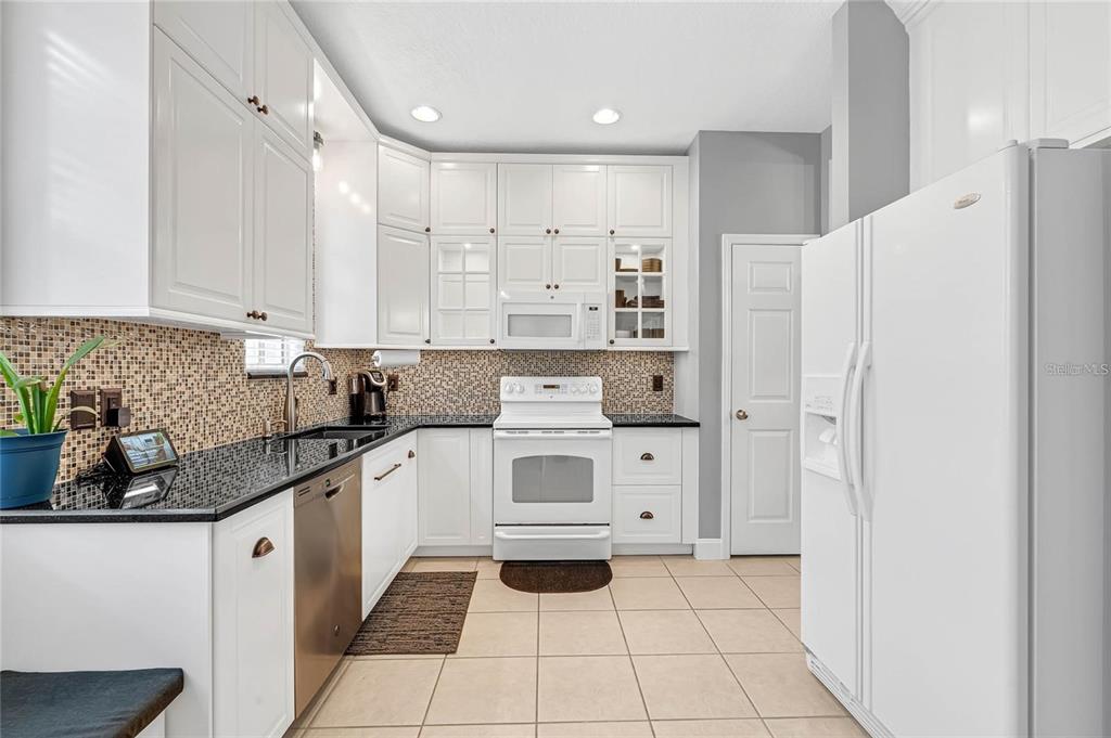 A kitchen features white cabinets, black countertops, a mosaic tile backsplash, and white appliances — 12543 CRUXBURY DRIVE, WINDERMERE, FL