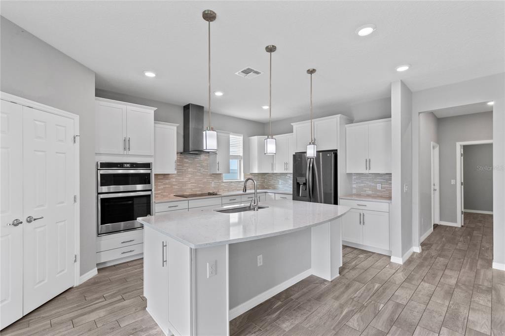 A modern kitchen features white cabinetry, a large quartz-topped island, stainless steel appliances, and wood-look flooring — 2754 MATERA DRIVE, ST CLOUD, FL