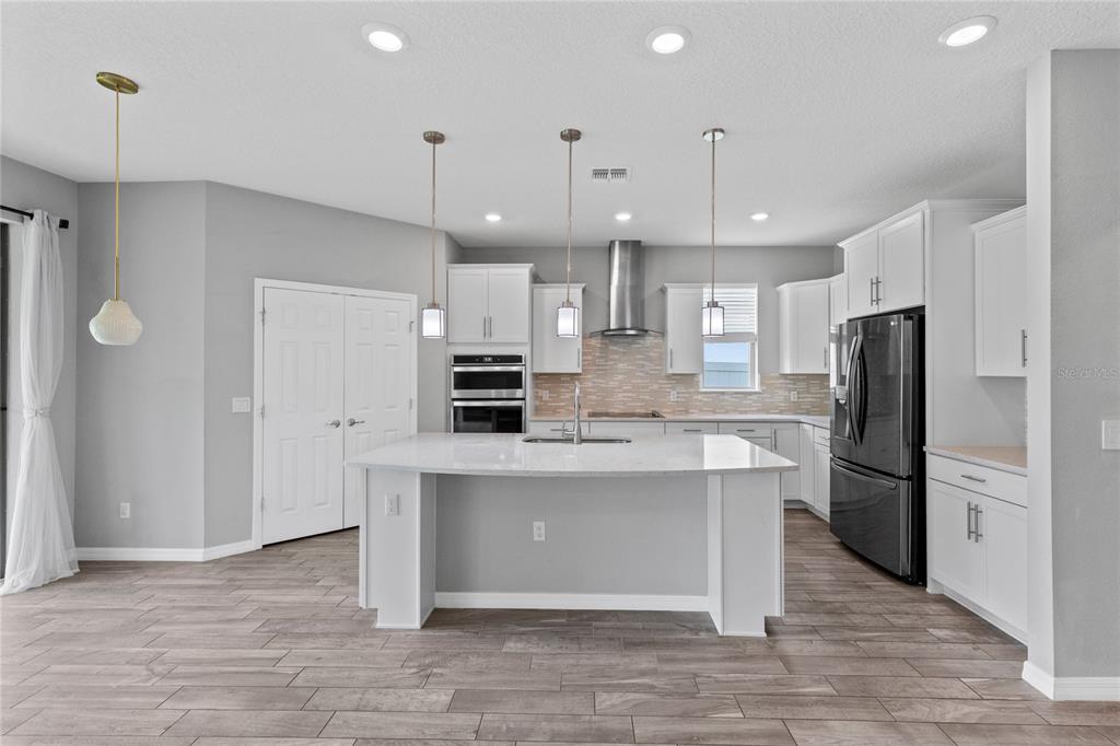 A modern kitchen features white cabinetry, a large central island, and stainless steel appliances — 2754 MATERA DRIVE, ST CLOUD, FL