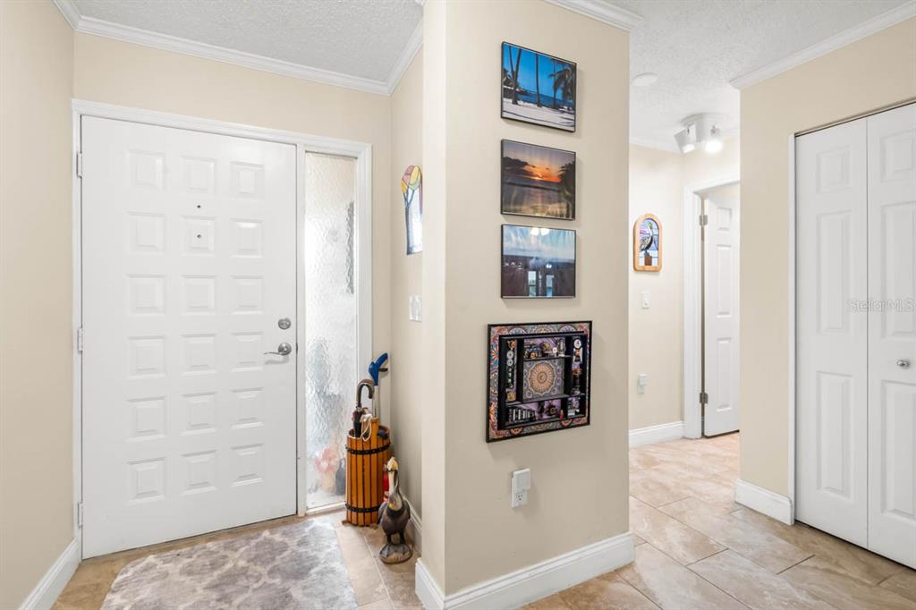 An entryway with a white front door, tiled floors, and wall-mounted artwork on a central pillar — 2519 LONIGAN PLACE, SUN CITY CENTER, FL