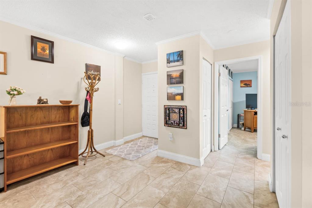 An entryway with tile flooring, a wooden bookshelf, a coat rack, and a hallway entrance — 2519 LONIGAN PLACE, SUN CITY CENTER, FL