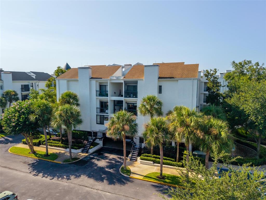 An exterior view of a multi-story white apartment building surrounded by palm trees and landscaping — 250 CAROLINA AVENUE UNIT 205, WINTER PARK, FL