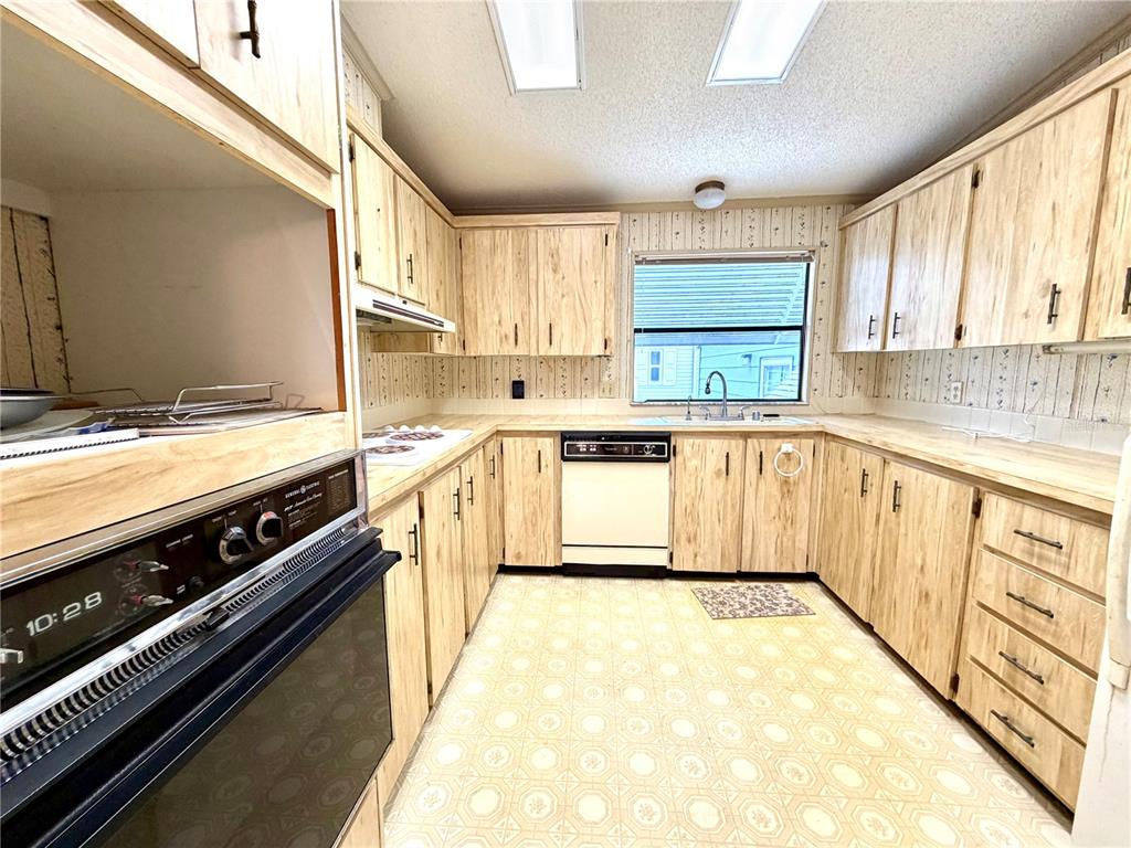 A kitchen features light wood cabinets, laminate countertops, a dishwasher, and patterned vinyl flooring — 3014 RAINBOW ROAD, TAVARES, FL