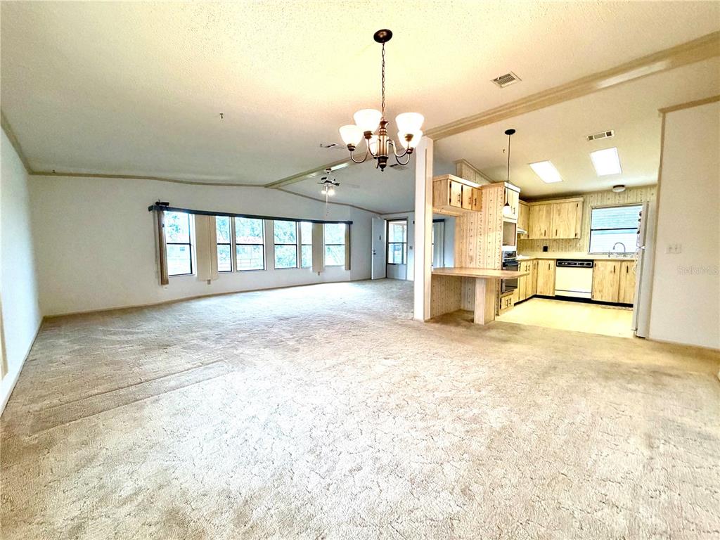A spacious living room with beige carpet opens into a kitchen with light wood cabinets — 3014 RAINBOW ROAD, TAVARES, FL