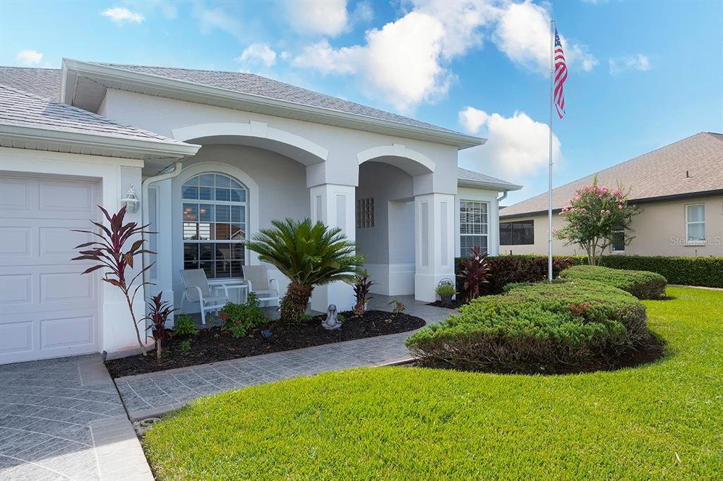 The exterior of a single-story house features a paved walkway, landscaping, and an American flag — 6112 90TH AVENUE CIRCLE E, PARRISH, FL