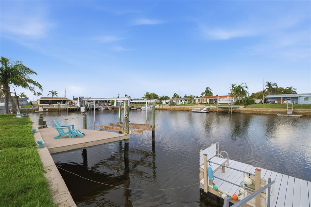 A canal view features two wooden docks, a boat lift, and blue Adirondack chairs — 12816 4TH ISLE, HUDSON, FL