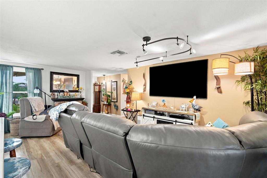 A living room features a grey sectional sofa, a wall-mounted television, and wood-look flooring — 12816 4TH ISLE, HUDSON, FL