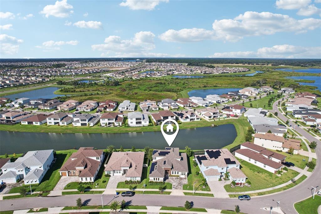 An aerial view shows a suburban house with solar panels overlooking a pond — 8743 SANDERS TREE LOOP, WESLEY CHAPEL, FL