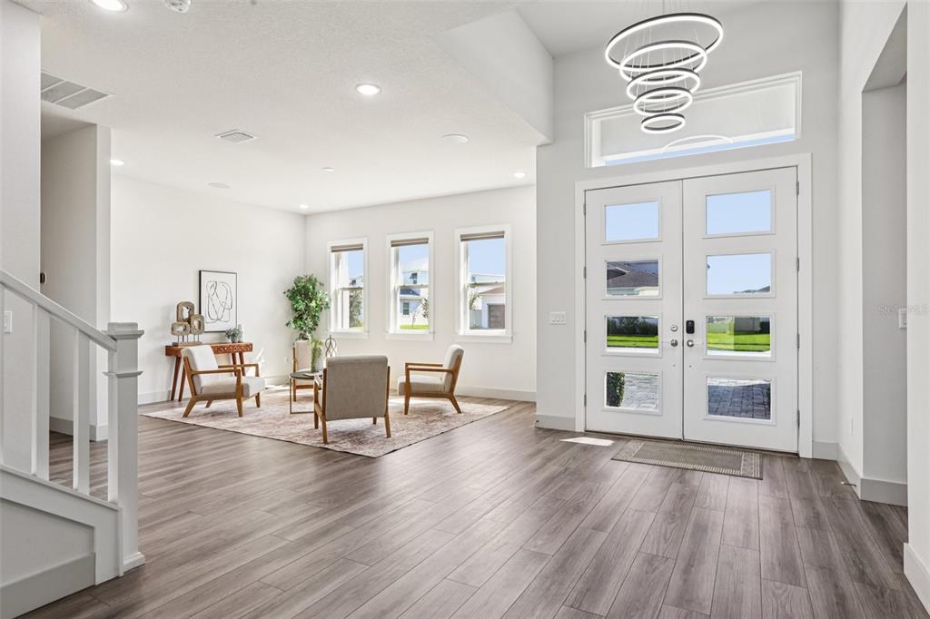 A bright entryway features wood-look flooring, a modern chandelier, and a seating area with windows — 8743 SANDERS TREE LOOP, WESLEY CHAPEL, FL