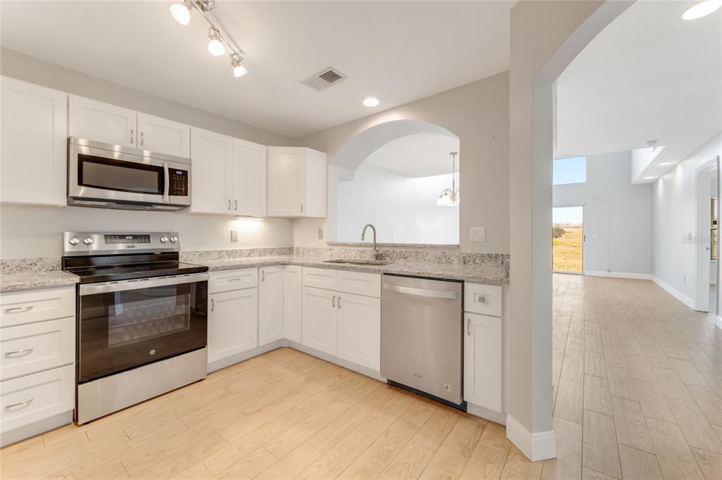 A kitchen with white cabinets, granite countertops, stainless steel appliances, and light wood-look flooring — 3070 OCEAN SHORE BOULEVARD, ORMOND BEACH, FL