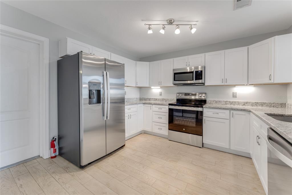A kitchen features white cabinets, stainless steel appliances, granite countertops, and light wood-look flooring — 3070 OCEAN SHORE BOULEVARD, ORMOND BEACH, FL