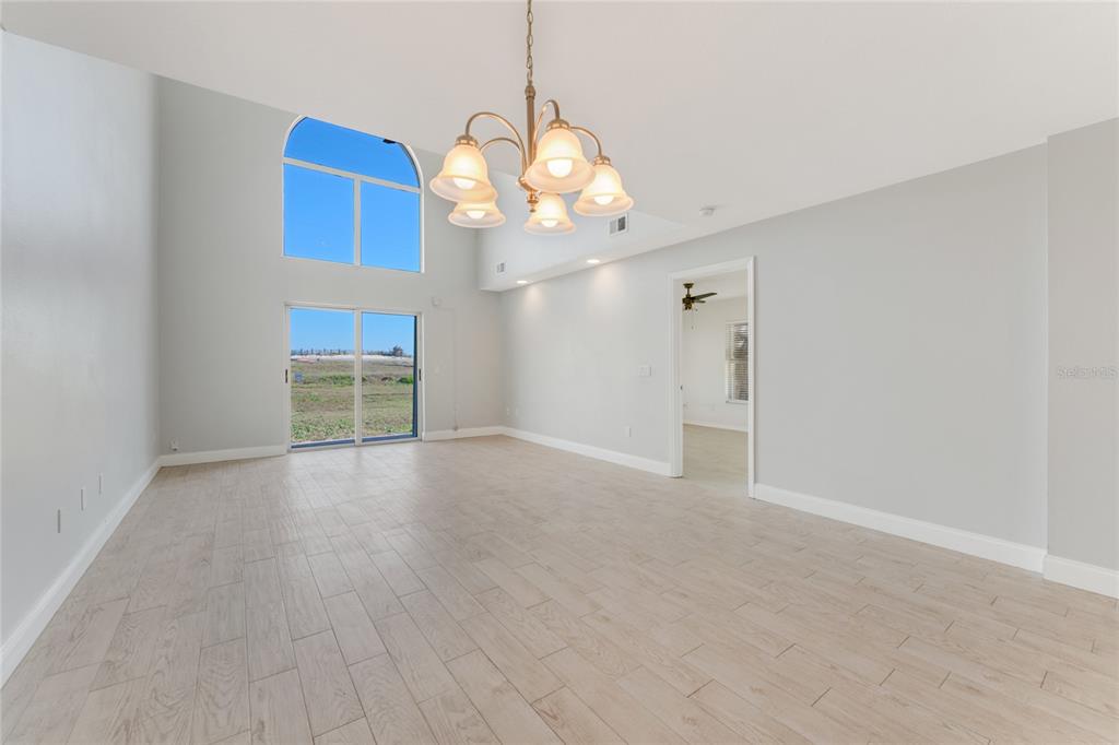 A bright, empty living room features high ceilings, a chandelier, and light-colored wood-look tile flooring — 3070 OCEAN SHORE BOULEVARD, ORMOND BEACH, FL