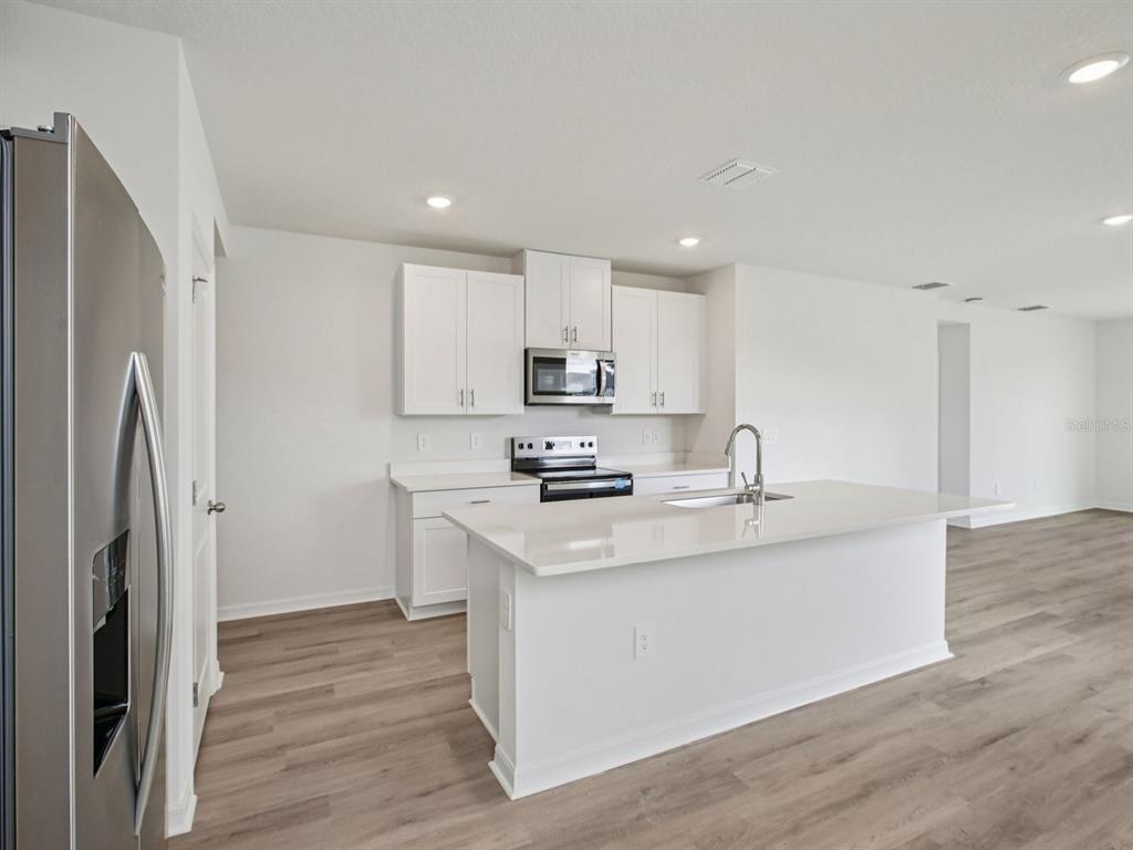 A modern kitchen features white cabinets, stainless steel appliances, and a central quartz island — 3744 MOSCATO DRIVE, BROOKSVILLE, FL