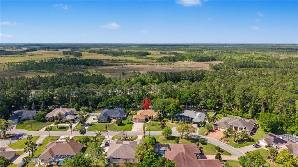 An aerial view shows a suburban neighborhood with houses surrounded by trees and open fields — 11 CRESCENT LAKE WAY, ORMOND BEACH, FL