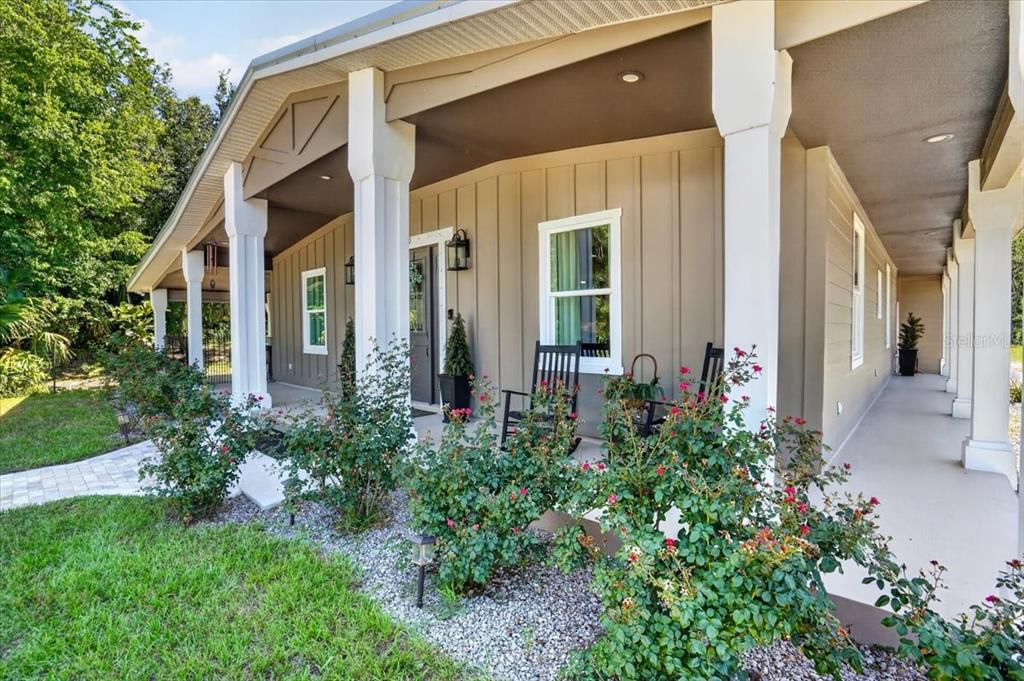 A covered front porch with white columns, rocking chairs, and rose bushes in front — 11740 DARSEY ROAD, PARRISH, FL
