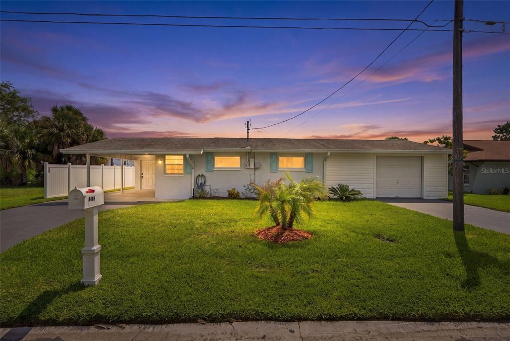 A single-story white house with a carport, garage, and a front lawn at dusk — 4496 BIMINI DRIVE, HERNANDO BEACH, FL
