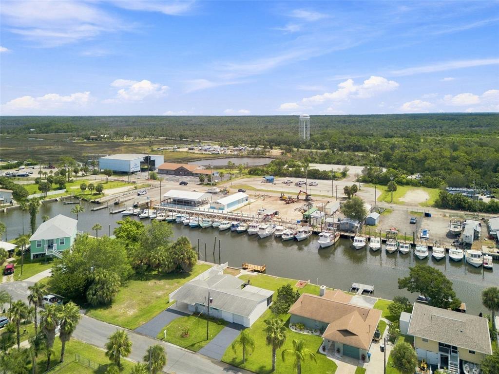 An aerial view shows a canal lined with boats, nearby houses, and a large industrial building — 4496 BIMINI DRIVE, HERNANDO BEACH, FL
