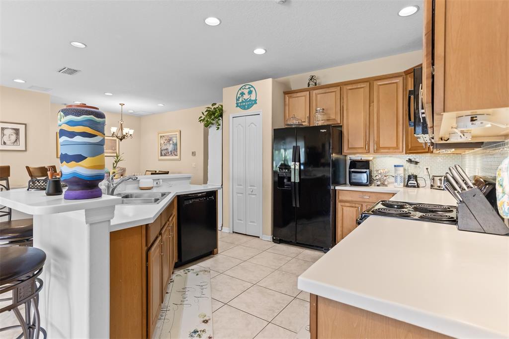 A kitchen features light wood cabinets, white countertops, black appliances, and tile flooring — 905 PARKER DEN DRIVE, RUSKIN, FL