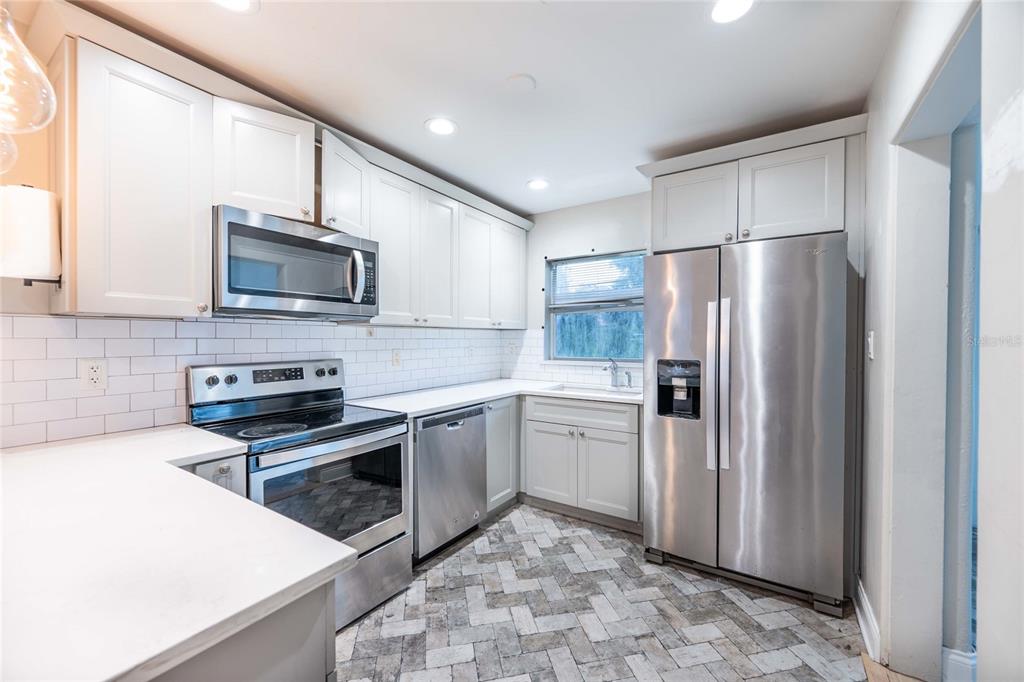 A kitchen with white cabinets, stainless steel appliances, white countertops, and a herringbone tile floor — 230 STRATHY LANE, WINTER PARK, FL
