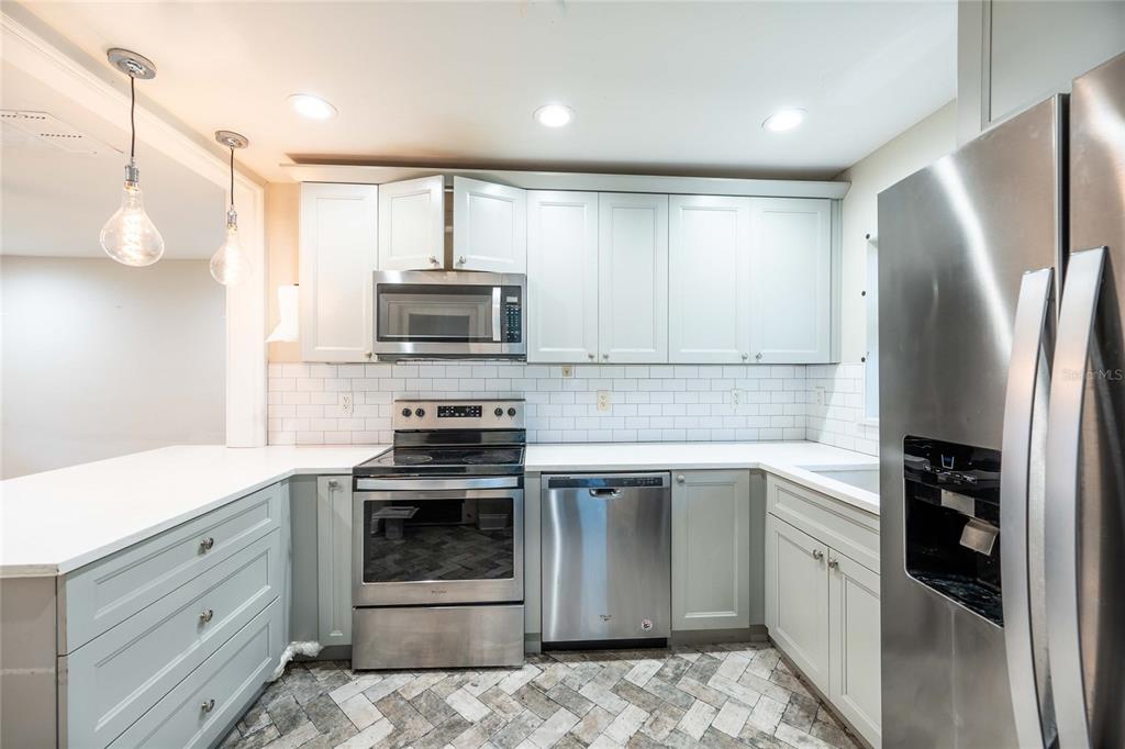 A kitchen features light gray cabinets, stainless steel appliances, white countertops, and a herringbone-patterned floor — 230 STRATHY LANE, WINTER PARK, FL