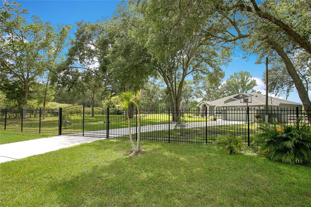 A gated driveway leads to a single-story house surrounded by mature trees and green lawn — 19616 LIVINGSTON AVENUE, LUTZ, FL