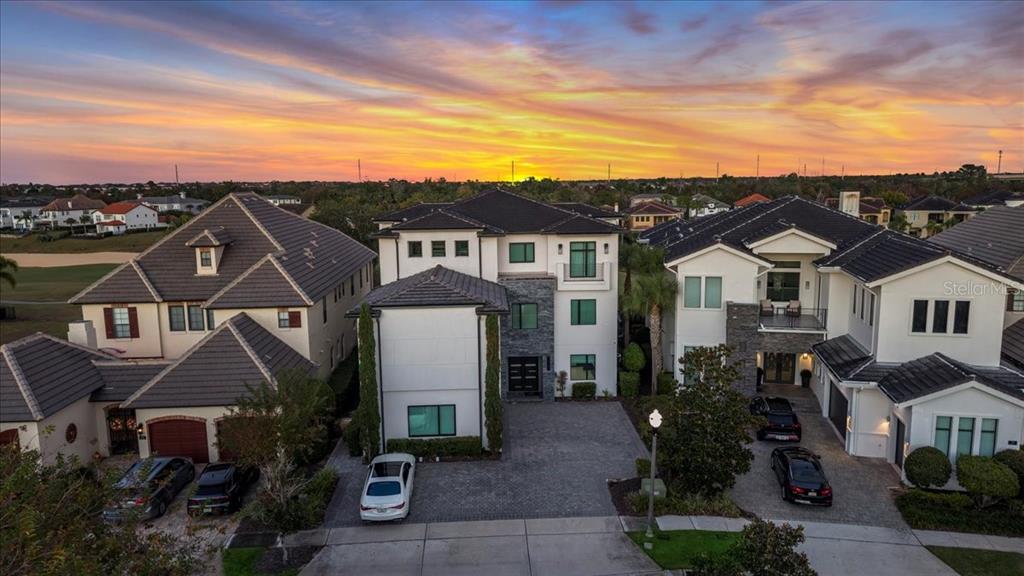 An aerial view shows three modern suburban houses with paved driveways at sunset — 331 MUIRFIELD LOOP, REUNION, FL