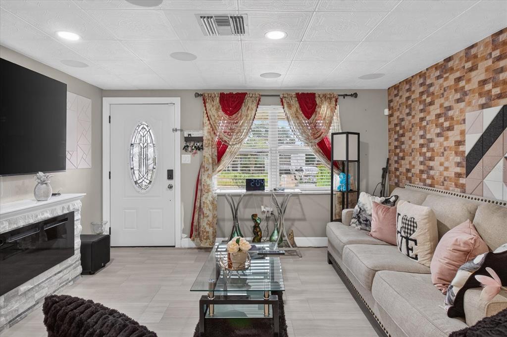 A living room features a fireplace, a beige sofa, a glass coffee table, and patterned curtains — 1031 CONOLEY LANE, HOLIDAY, FL
