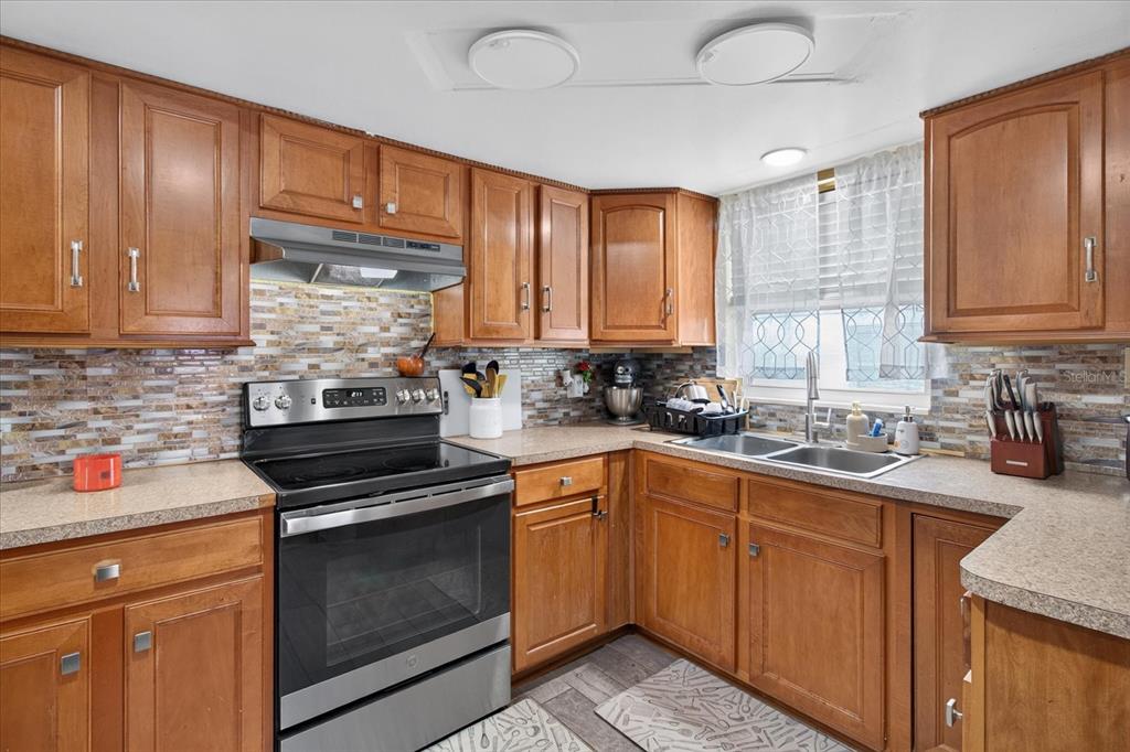 A kitchen with wood cabinets, stainless steel appliances, a tiled backsplash, and laminate countertops — 1031 CONOLEY LANE, HOLIDAY, FL