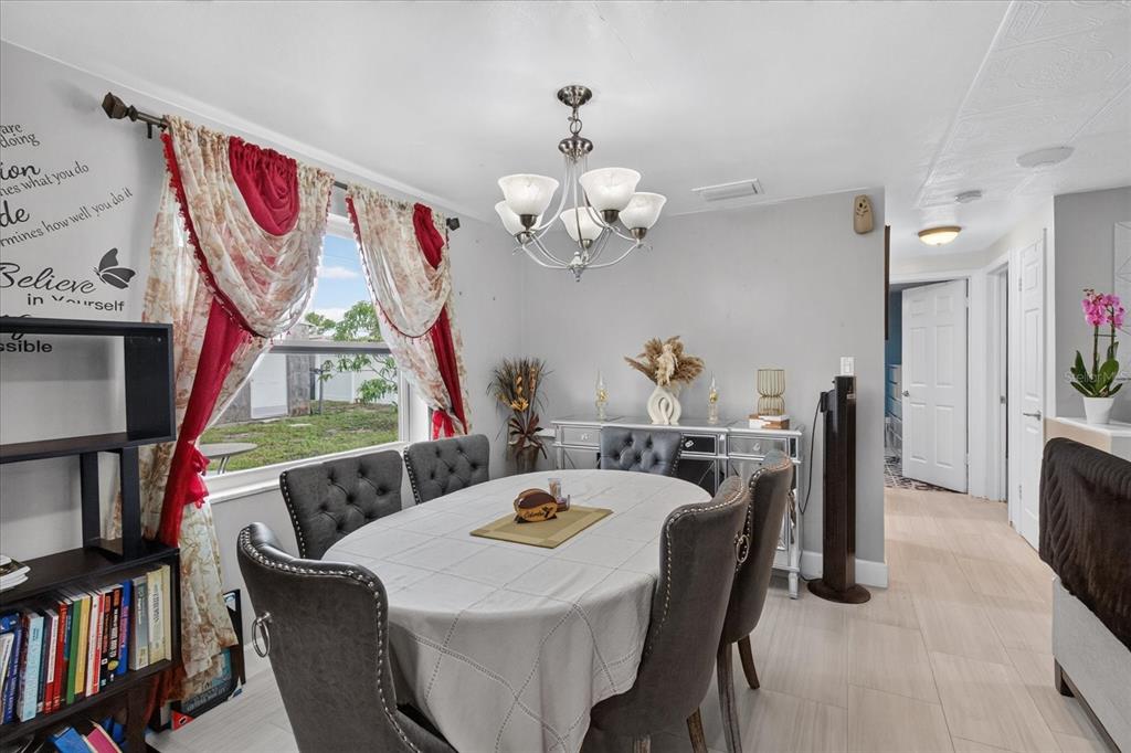 A dining room features a gray tufted chair set, a chandelier, and red-accented window curtains — 1031 CONOLEY LANE, HOLIDAY, FL