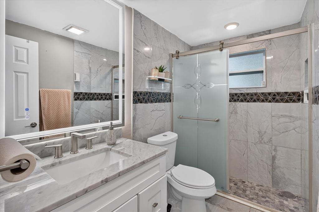 A bathroom features a marble vanity, a walk-in shower with glass doors, and gray tile — 1031 CONOLEY LANE, HOLIDAY, FL