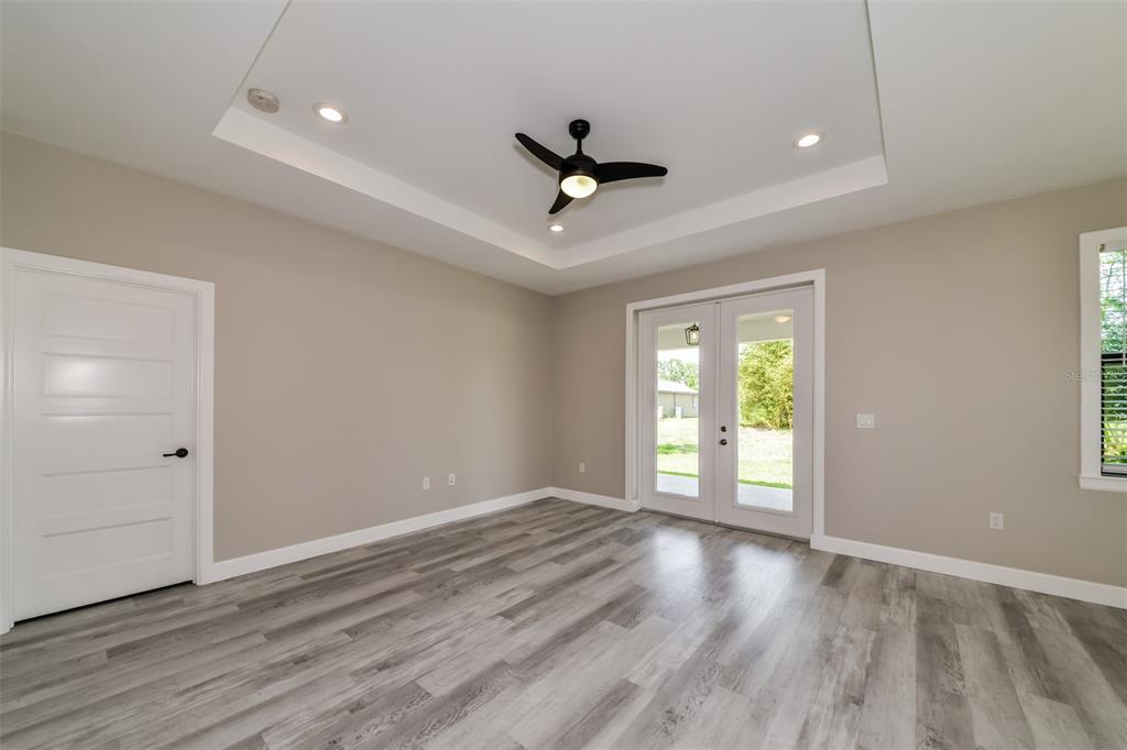 A room with gray wood-look flooring, a tray ceiling with a fan, and glass doors — 2646 MORRIETTA LANE, NORTH PORT, FL