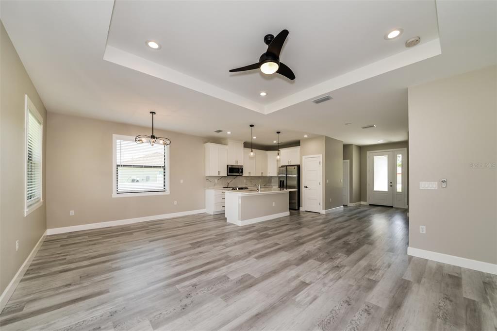 An open-concept living and kitchen area features light wood-look flooring and a tray ceiling — 2646 MORRIETTA LANE, NORTH PORT, FL