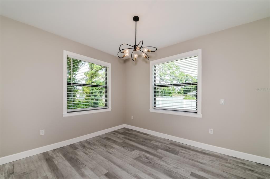 An empty room features light gray walls, wood-look flooring, two windows, and a modern chandelier — 2646 MORRIETTA LANE, NORTH PORT, FL