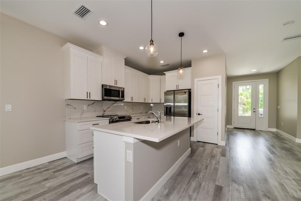 A modern kitchen features white cabinets, quartz countertops, a center island, and wood-look flooring — 2646 MORRIETTA LANE, NORTH PORT, FL