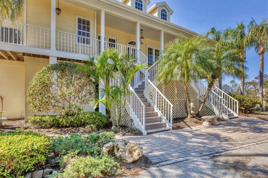 An elevated yellow house features a wide porch, white railings, and stairs leading to the entrance — 92 TIDY ISLAND BOULEVARD, BRADENTON, FL