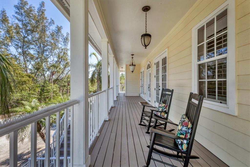 A covered wooden porch features two rocking chairs, white railings, and hanging light fixtures — 92 TIDY ISLAND BOULEVARD, BRADENTON, FL