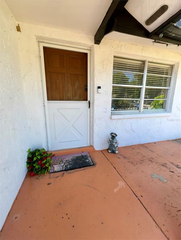 A white front door with a wooden top panel sits beside a window on a porch — 6432 JUNIPER ROAD, PORT RICHEY, FL