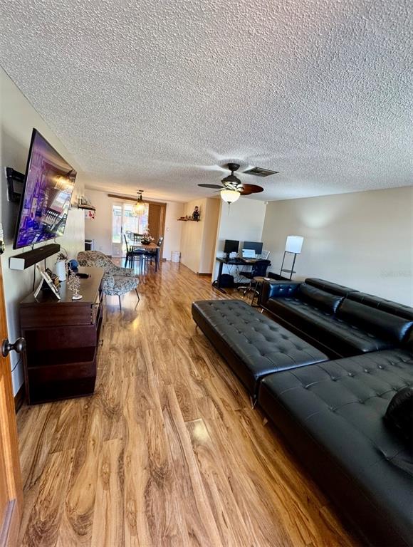 A living room features wood-look flooring, a large black sectional sofa, and a ceiling fan — 6432 JUNIPER ROAD, PORT RICHEY, FL
