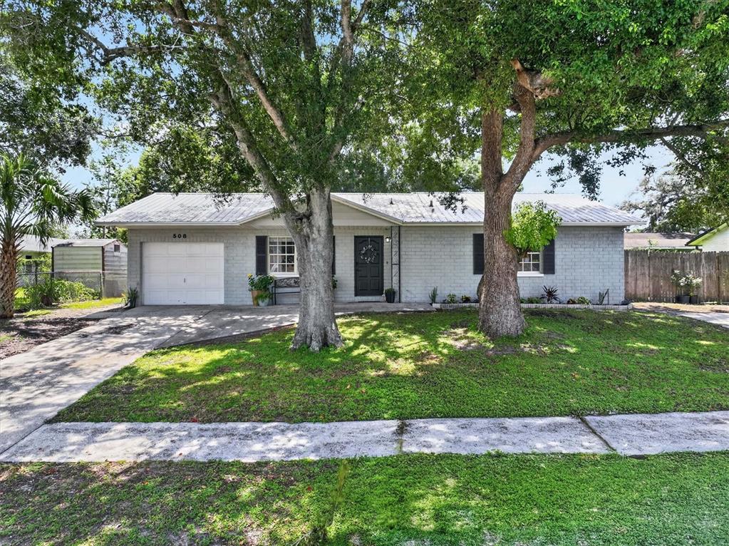 A single-story gray brick house with a metal roof and two large trees in front — 508 COCOPLUM DRIVE, SEFFNER, FL