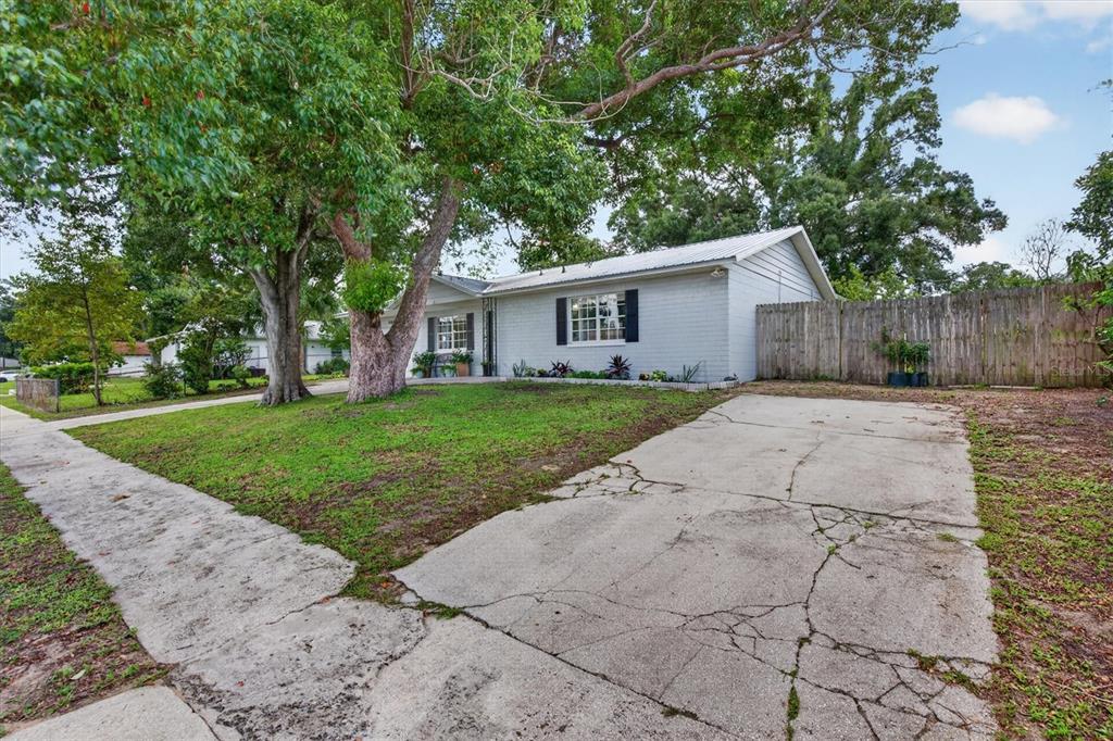 A single-story gray brick house with a cracked concrete driveway and large shade trees — 508 COCOPLUM DRIVE, SEFFNER, FL