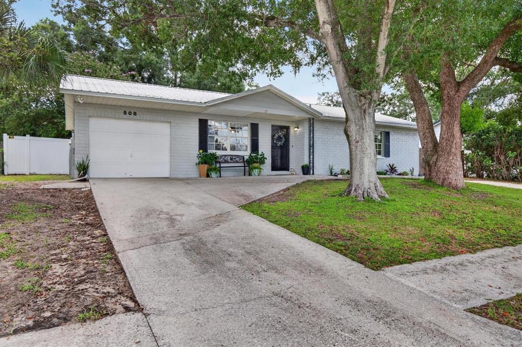 A single-story house with a white brick exterior, metal roof, and a concrete driveway — 508 COCOPLUM DRIVE, SEFFNER, FL